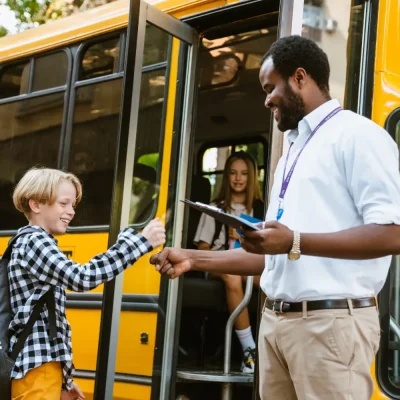 a man shaking hands with a boy in front of a school bus